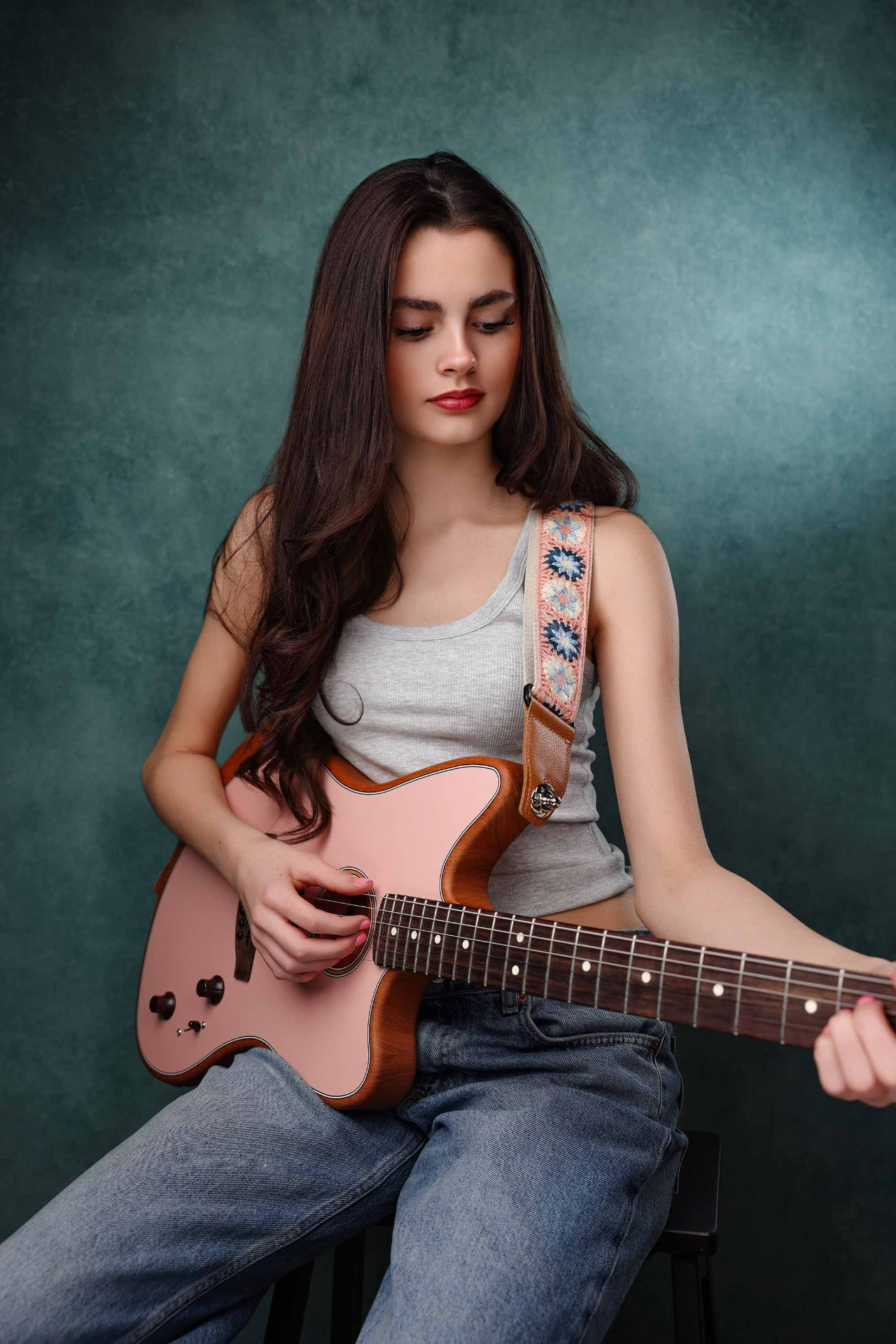 Ellie Gray seated with a pink electric guitar against a teal backdrop