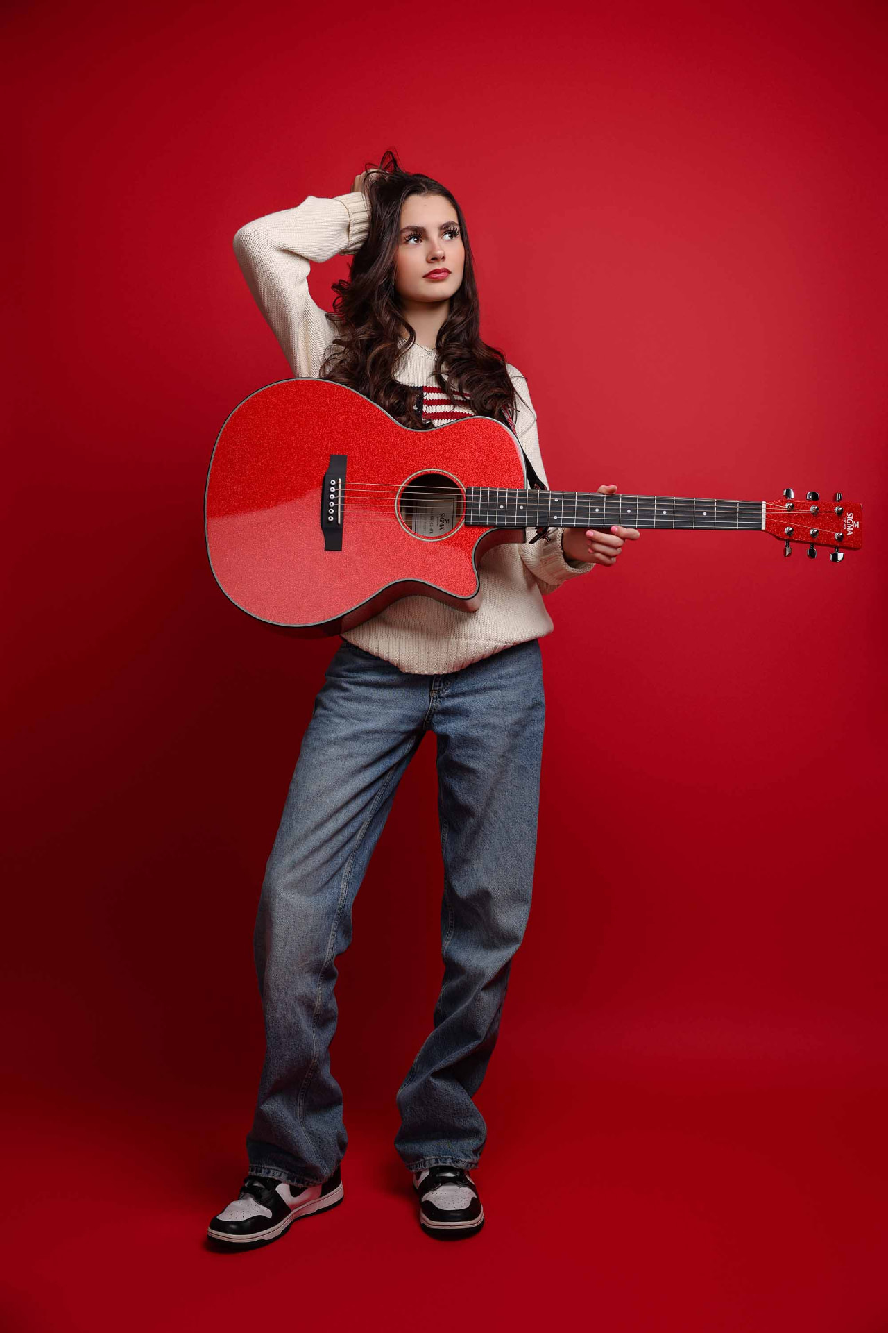 Ellie Gray holding a red sparkle acoustic guitar against a red backdrop