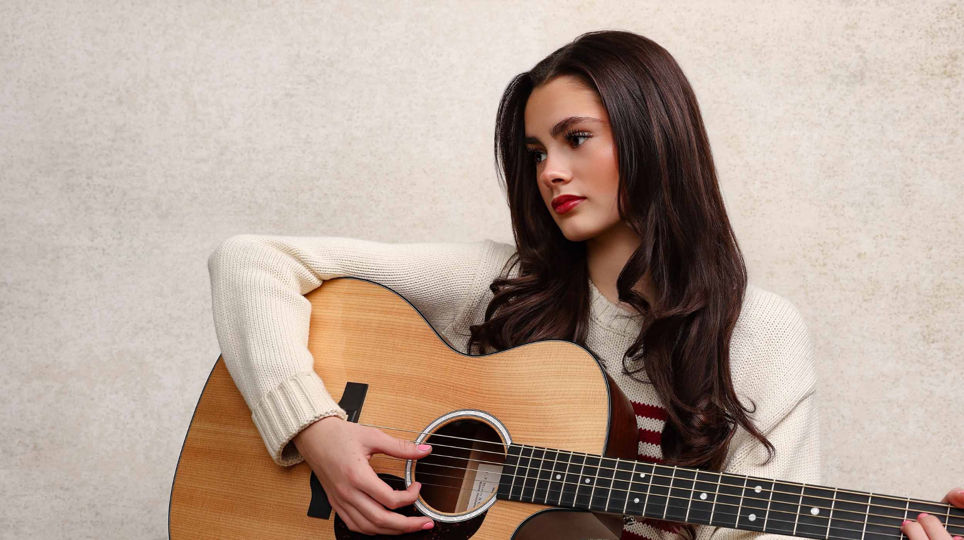 Ellie Gray standing in a dark studio holding an acoustic guitar