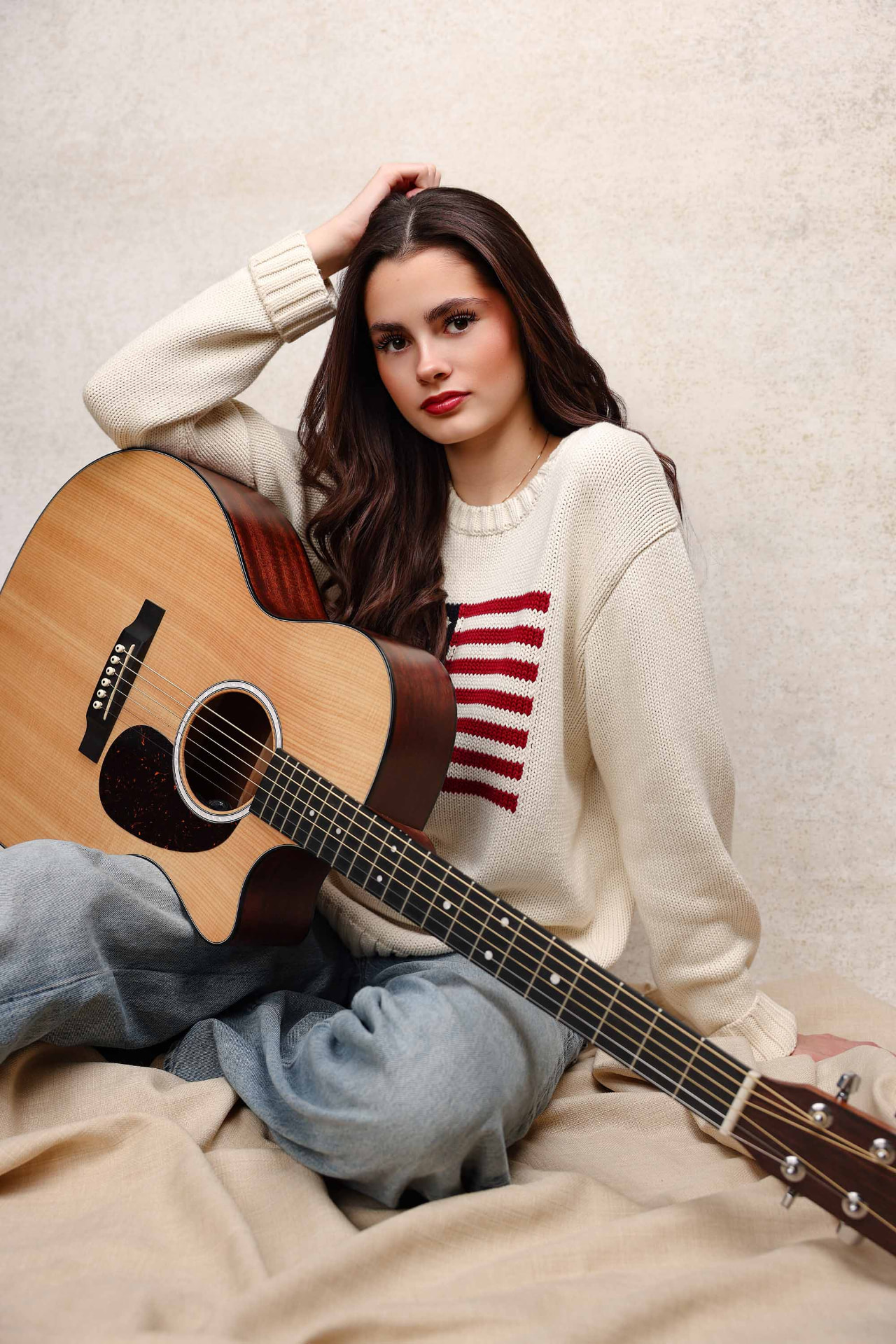 Ellie Gray seated in a cream striped sweater with an acoustic guitar against a neutral backdrop