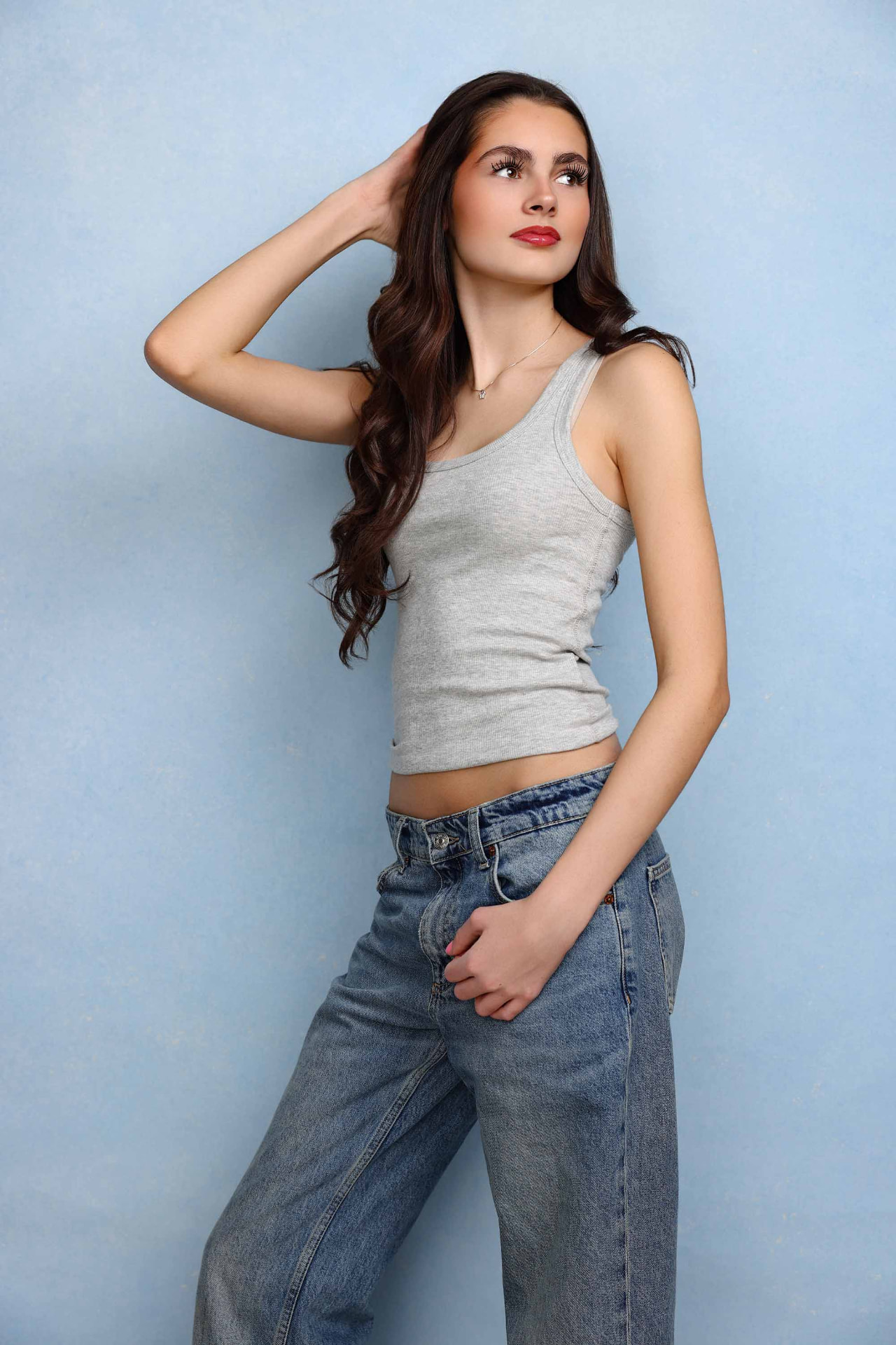 Ellie Gray standing in a grey vest and denim against a blue backdrop