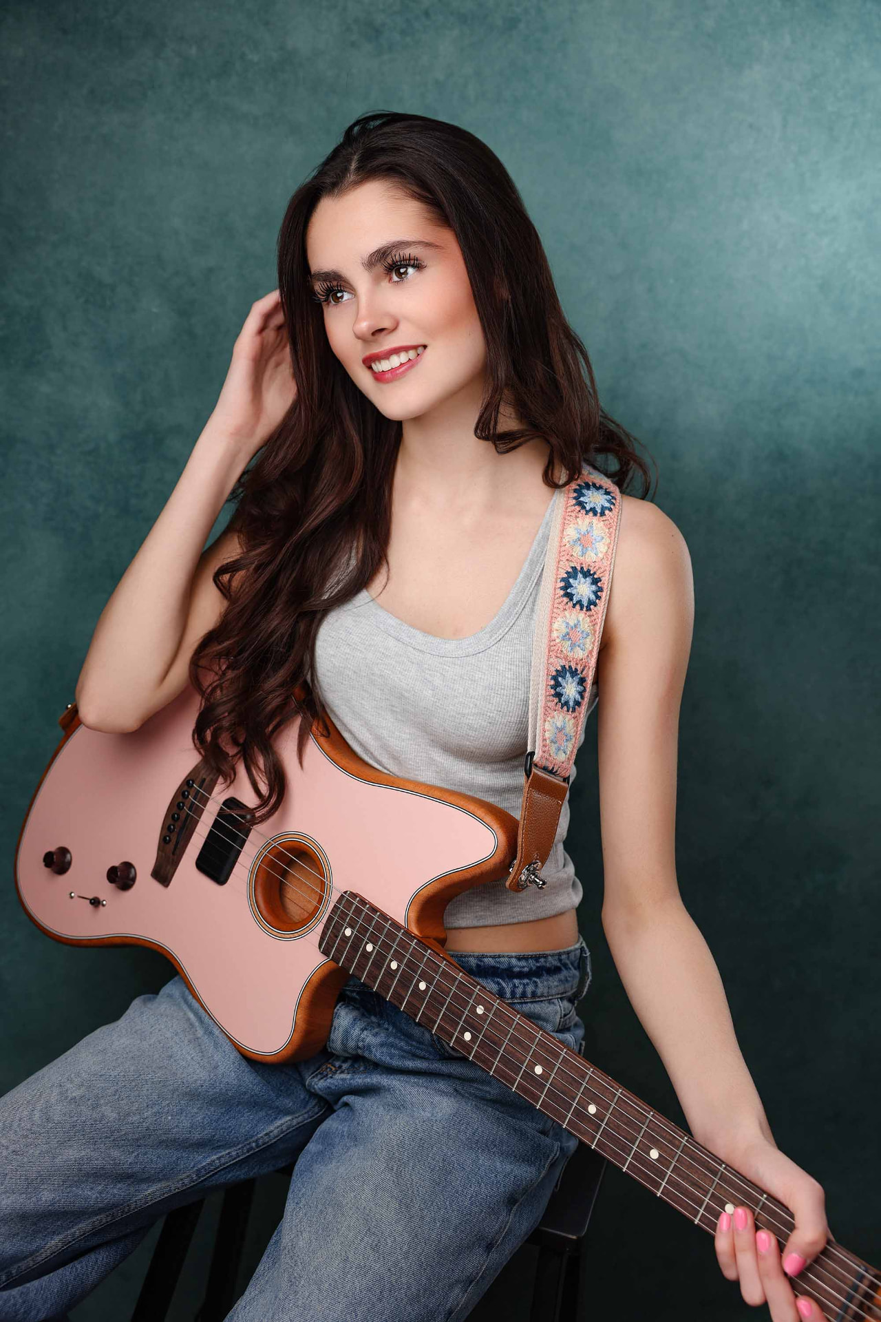 Ellie Gray smiling with a pink electric guitar against a teal backdrop